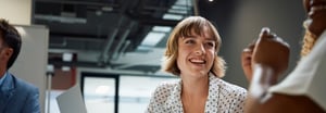 Woman with blonde bob in a white polka dot top smiling at coworker with laptop in front of them