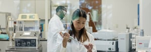 A female scientist in a white lab coat putting liquid into a vial