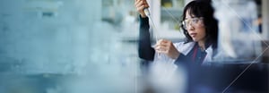 A female scientist in protective glasses putting liquid into a beaker