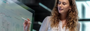 A woman holding a stylus and presenting a data analytics dashboard on a large screen.