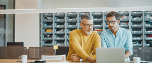 Two men with glasses pointing at a laptop
