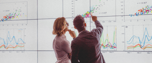 Two people interacting with a large screen displaying charts and data