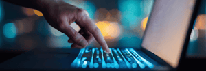 A close up of a hand hovering above a laptop keyboard with the index finger extended slightly, poised to press a key
