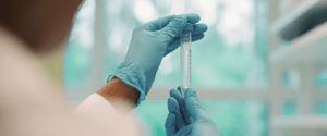 Gloved hands holding a capped tube filled with liquid