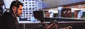 A camera operator wearing headphones operates a professional video camera in a broadcast studio setting.